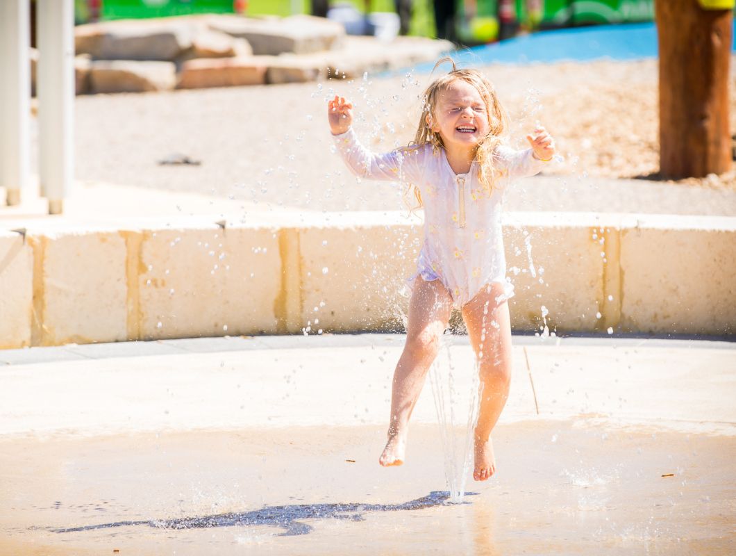 Allara, Eglinton young child smiling while enjoying the waterplay at Revolution park.