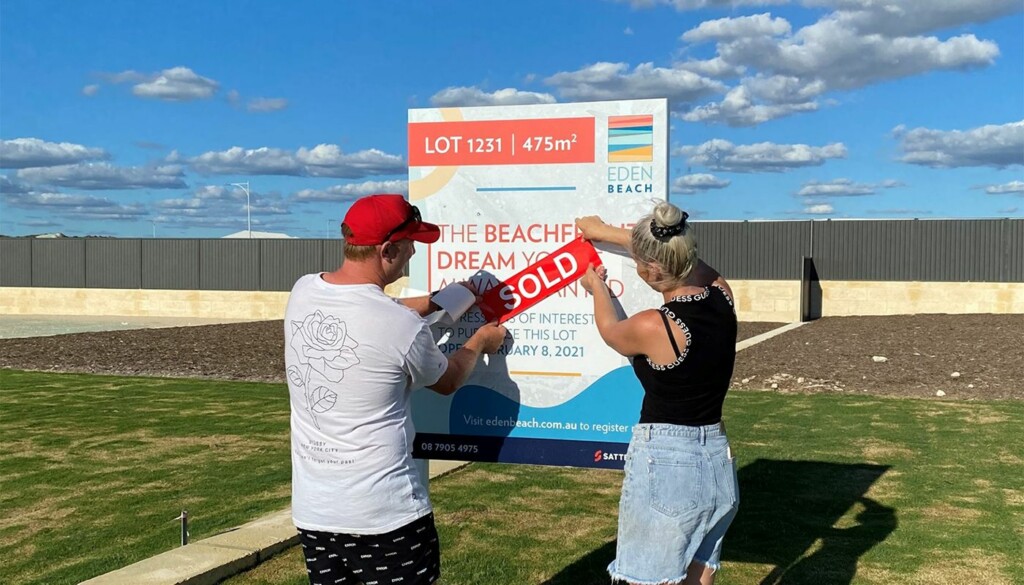 Eden Beach, Jindalee, young couple placing sold sticker on their dream lot