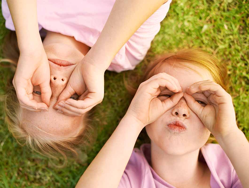 Two young children laying on the grass making faces with their hands over their eyes