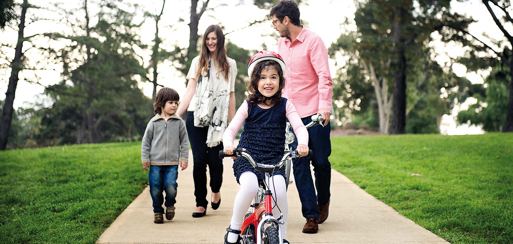 Young girl riding bike with her parents and younger sibling walking behind