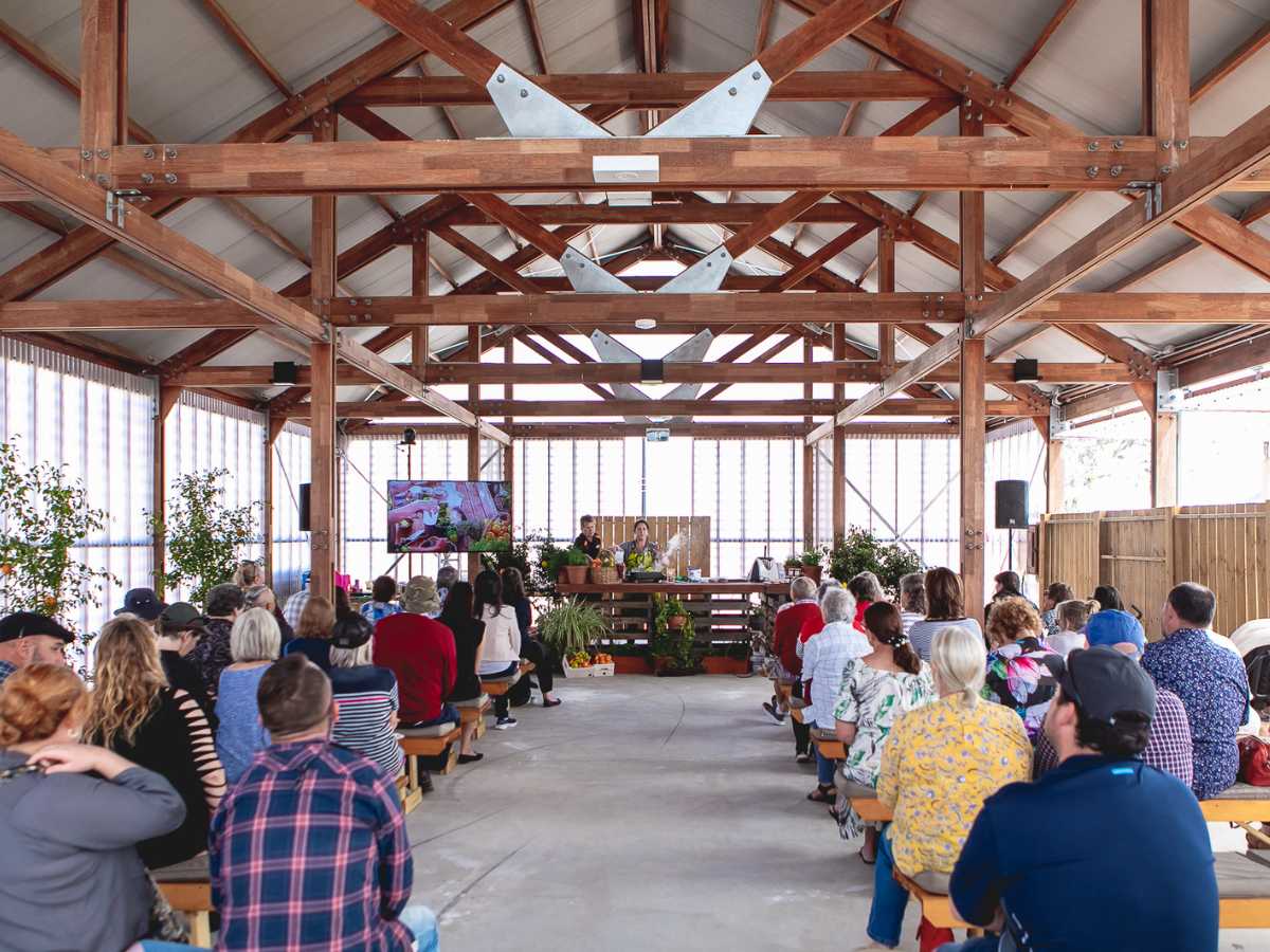 Seated audience watching a cooking demonstration in a rustic pavilion